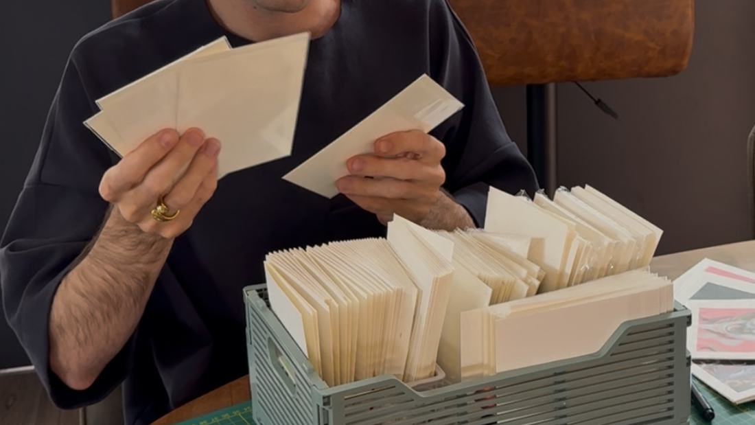 Man met verschillende art prints in zijn handen en een mandje met art prints voor zich.