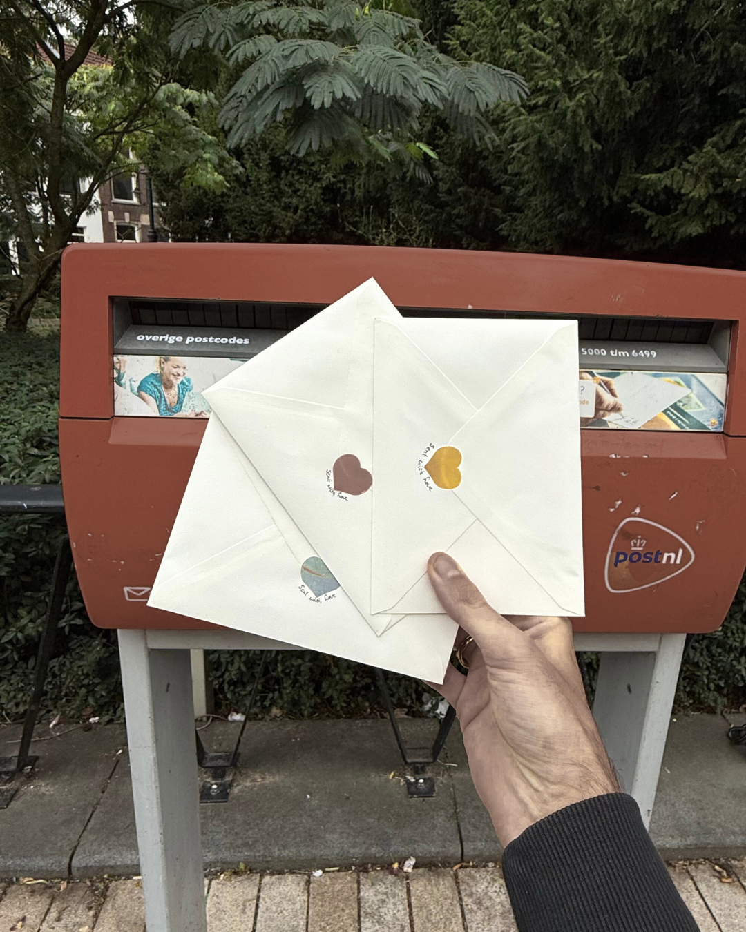 De eerste editie van de KOJO Art Print Club die op de post wordt gedaan. We zien enveloppen die zijn dichtgeplakt met een sticker in de vorm van een hartje voor een PostNL brievenbus, precies zoals snail mail wordt verzonden.